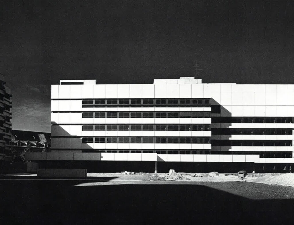 Modernes, mehrgeschossiges Verwaltungsgebäude mit horizontal gegliederter Fassade; Aufnahme während oder kurz nach der Bauphase, im Vordergrund unbefestigtes Gelände.